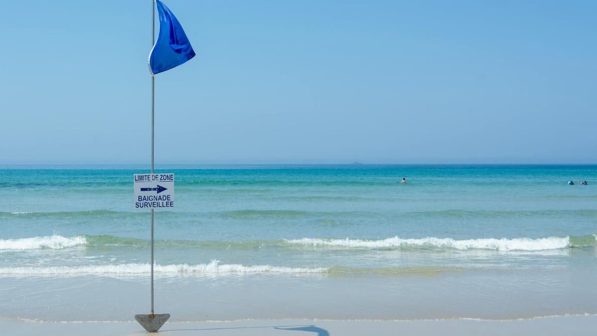 Tranquil beach with a blue flag and safety sign, perfect for summer travel.
