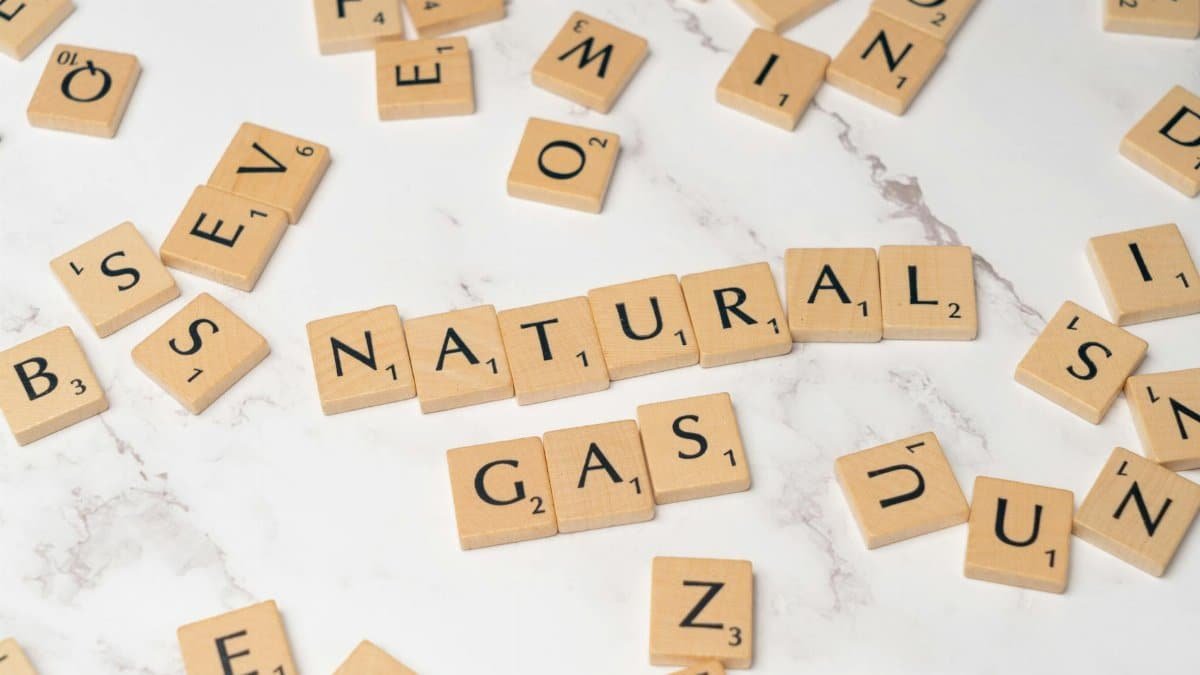 Wooden letter tiles on a marble surface spelling out 'natural gas' and scattered letters.