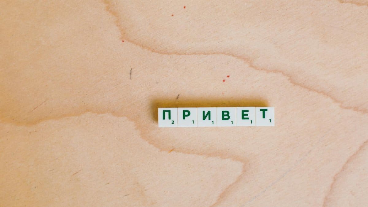 Scrabble tiles in Cyrillic spelling 'Hello' on a wooden surface.