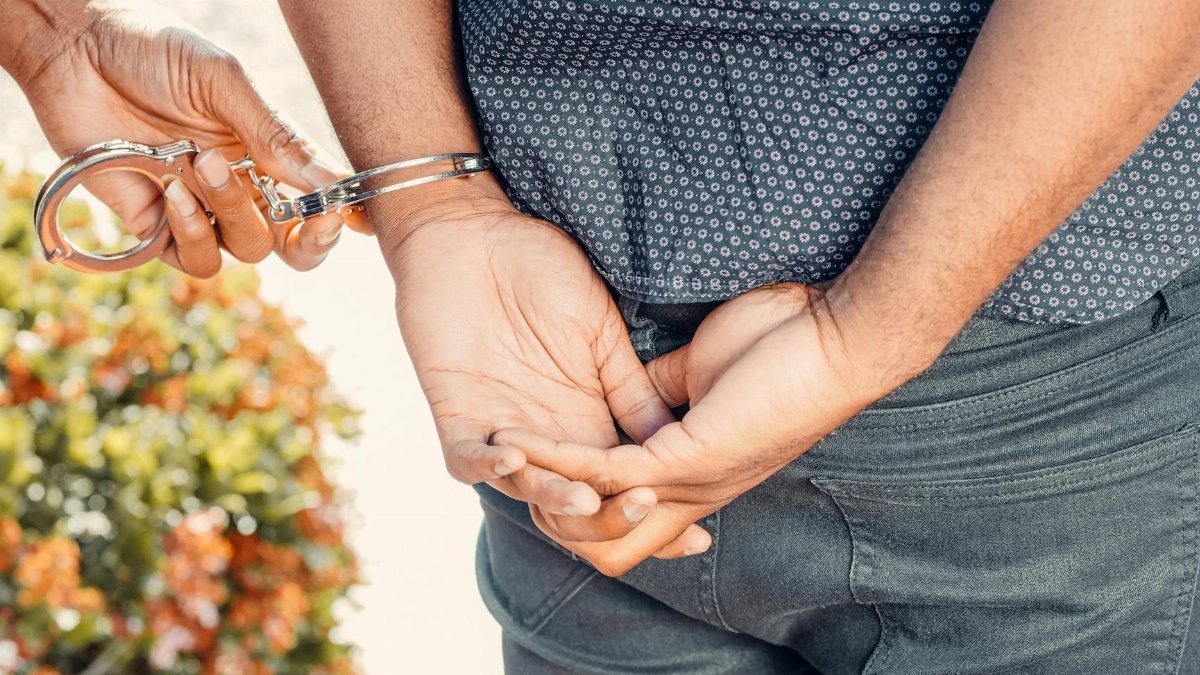 Close-up of hands in handcuffs during an arrest by police officer outdoors.