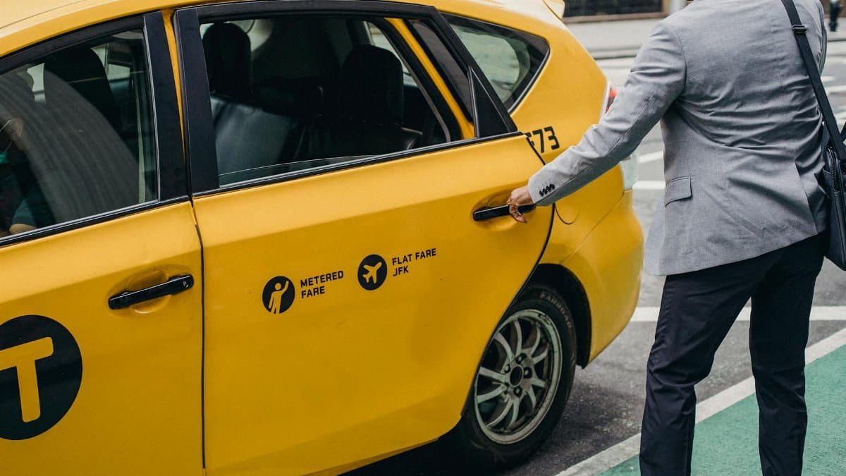 An urban businessman opens a yellow taxi door on a busy city street, showcasing modern commuting.