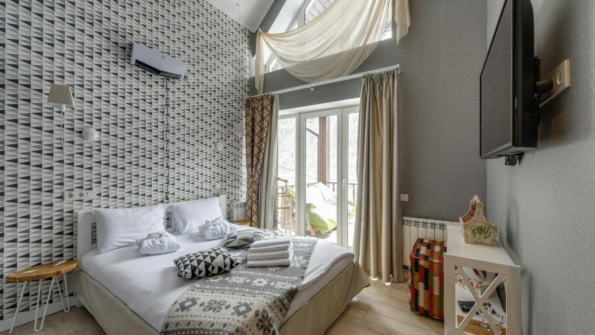 Bright and cozy modern bedroom featuring large windows, TV, and stylish decor.