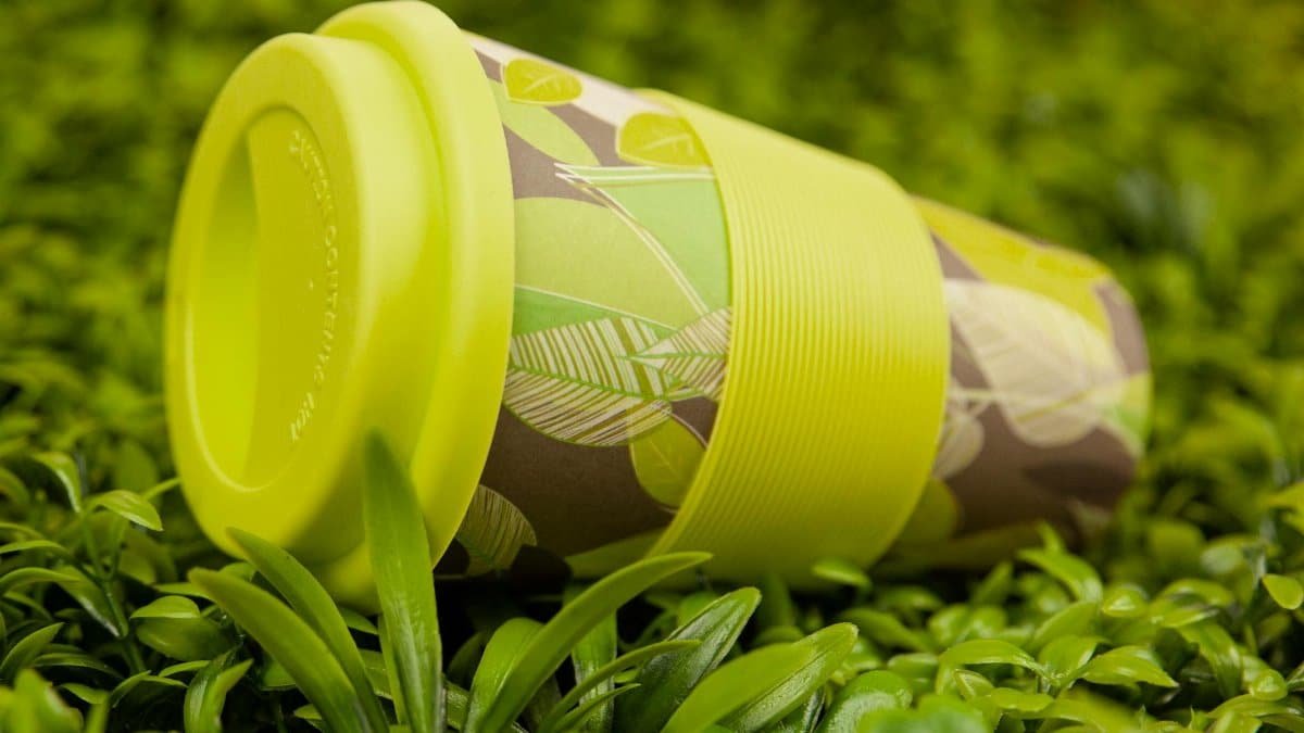 Bright green and patterned reusable cup amidst lush green leaves, showcasing sustainability.