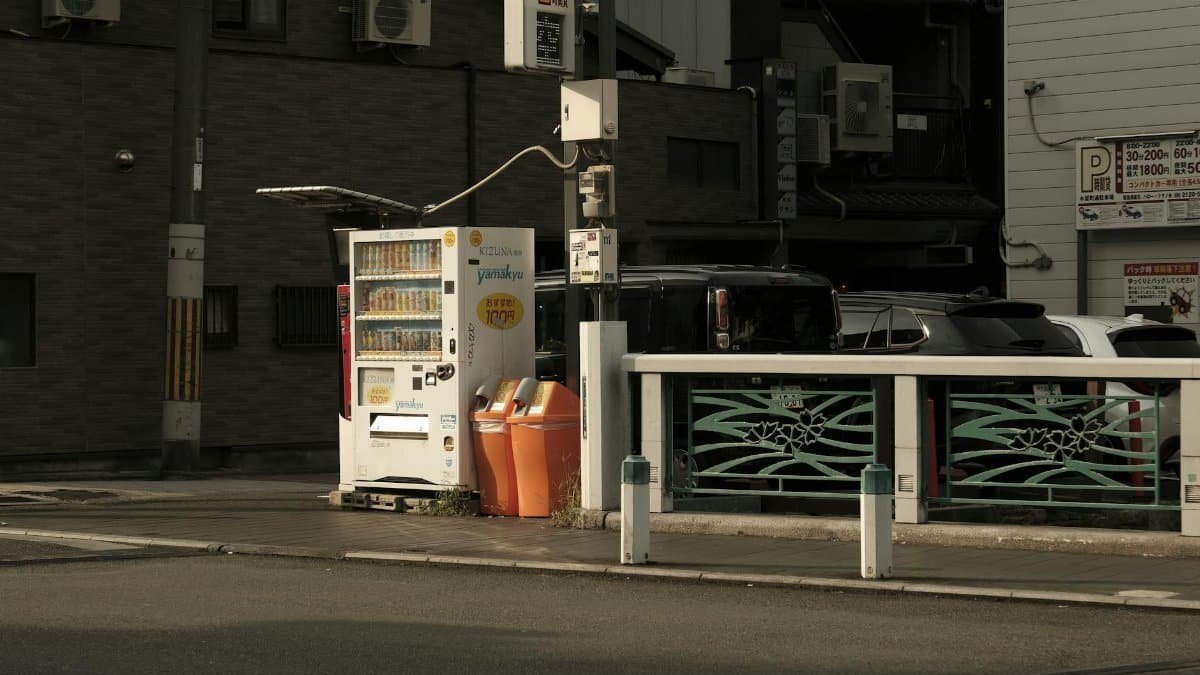 Urban street in Japan featuring a vending machine and parked cars in a quiet neighborhood.