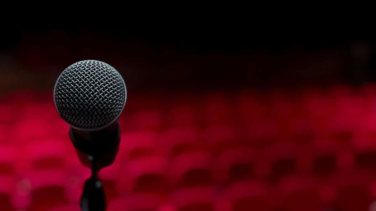 Close-up of microphone on stage with empty red seats in background.