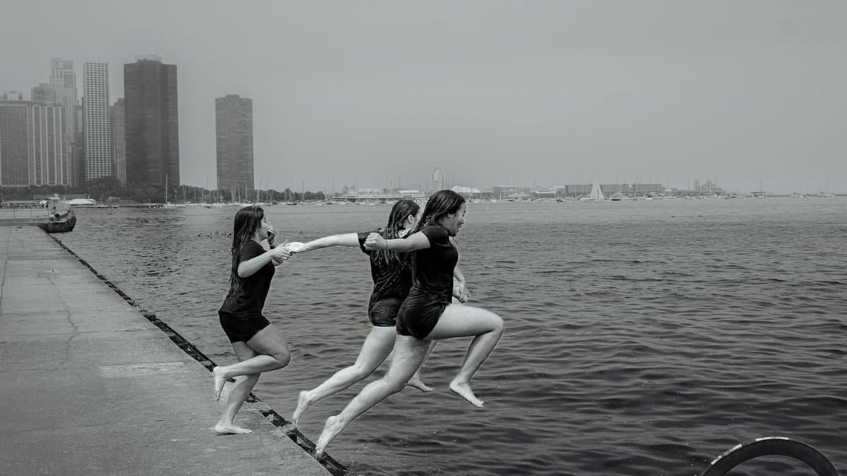Young women joyfully leap into Lake Michigan in Chicago, capturing a fun summer moment.