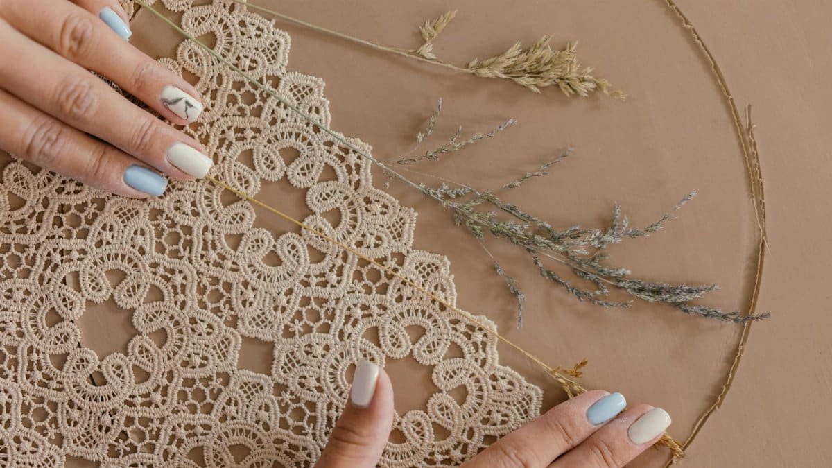 A close-up of handmade lace creation with delicate hands and colorful nails, showcasing intricate craftsmanship.