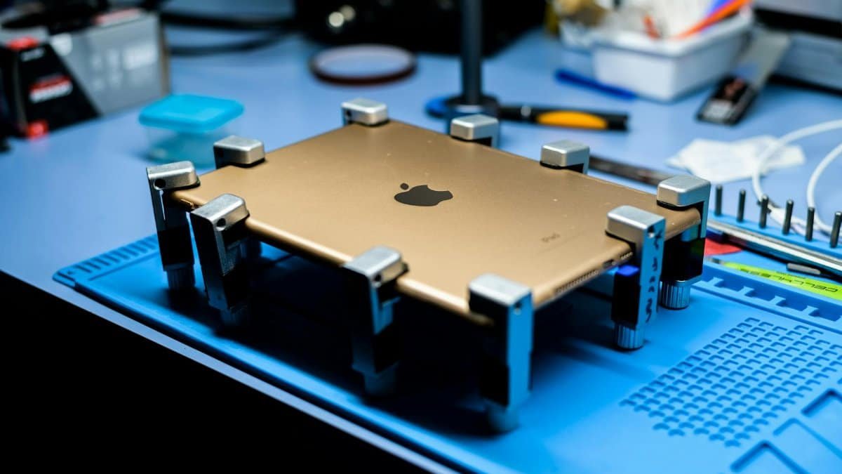 A close-up view of a tablet undergoing repair in a tech workshop with specialized tools.