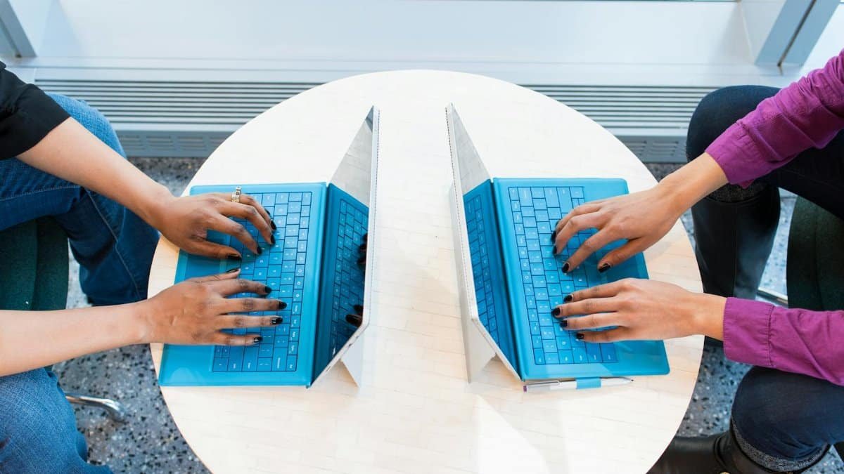Two people working on blue laptops at a round table, focusing on teamwork and technology.