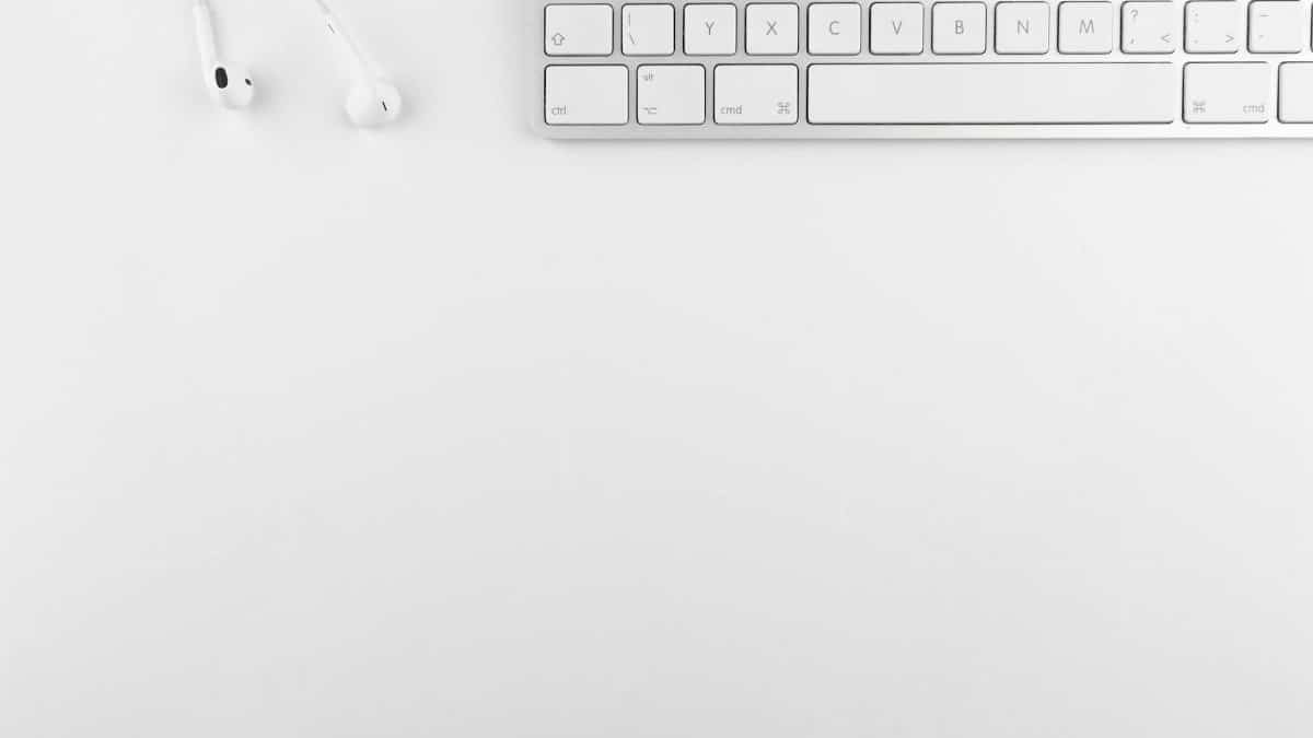 Top view of a white minimalist desk featuring a keyboard and earphones, ideal for technology themes.