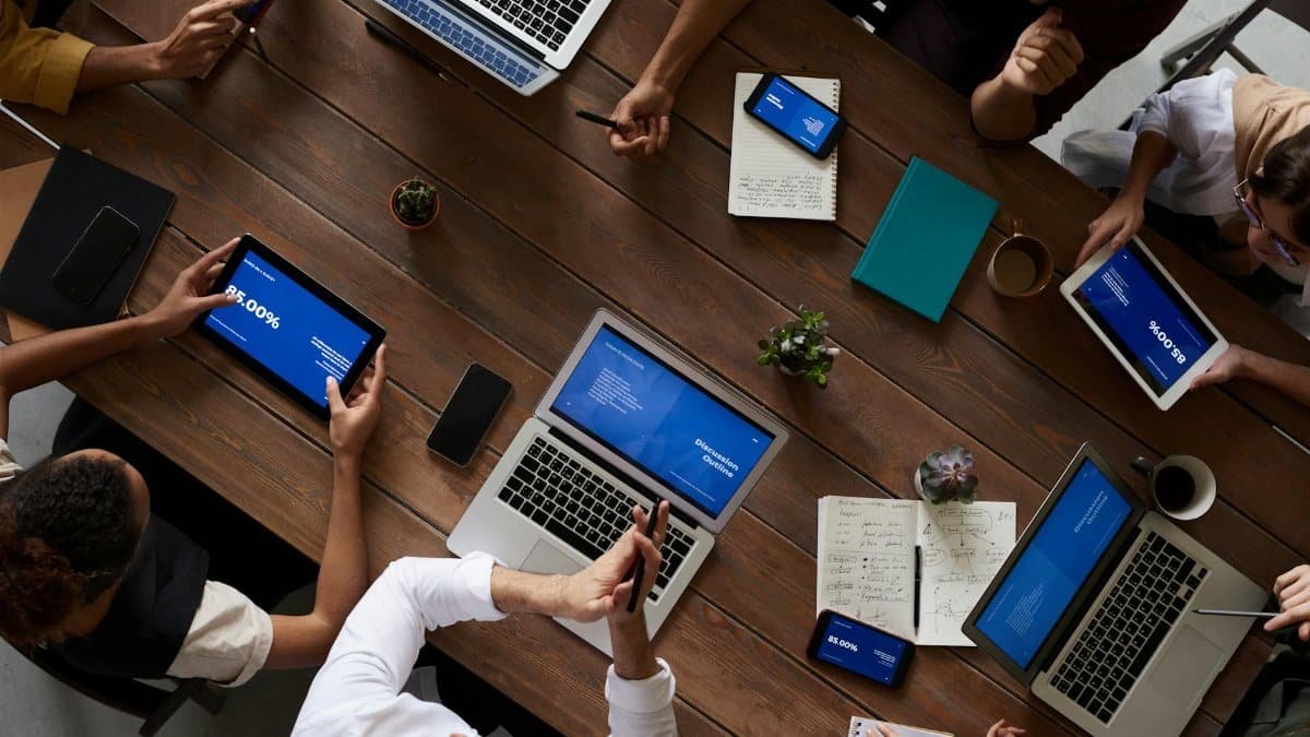 Overhead view of a diverse team discussing around a wooden table, using technology.