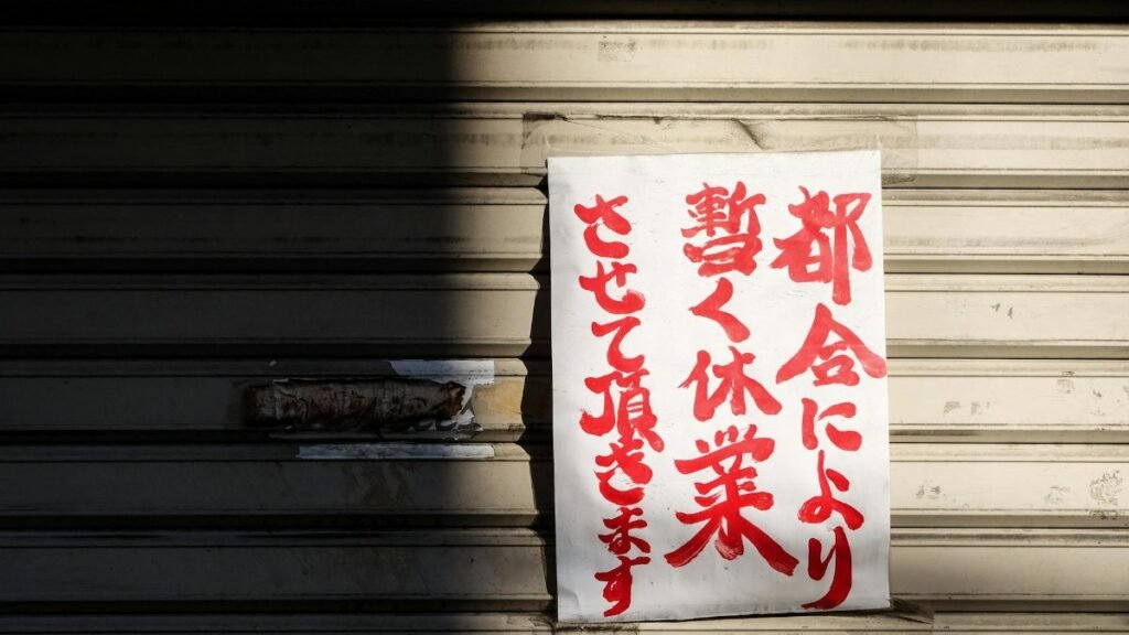A handwritten Japanese closure sign on a metal storefront shutter, partially shadowed.