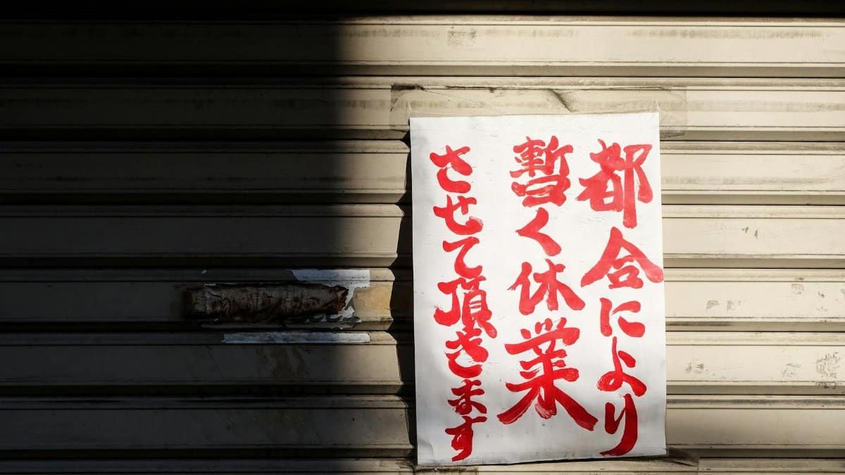A handwritten Japanese closure sign on a metal storefront shutter, partially shadowed.