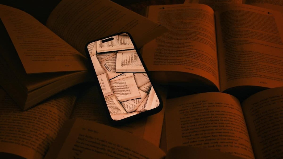 A smartphone displaying pages lies among open books, symbolizing digital integration.