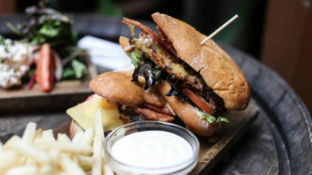 Close-up of a gourmet burger with fries, side salad, and dipping sauce in a rustic restaurant setting.