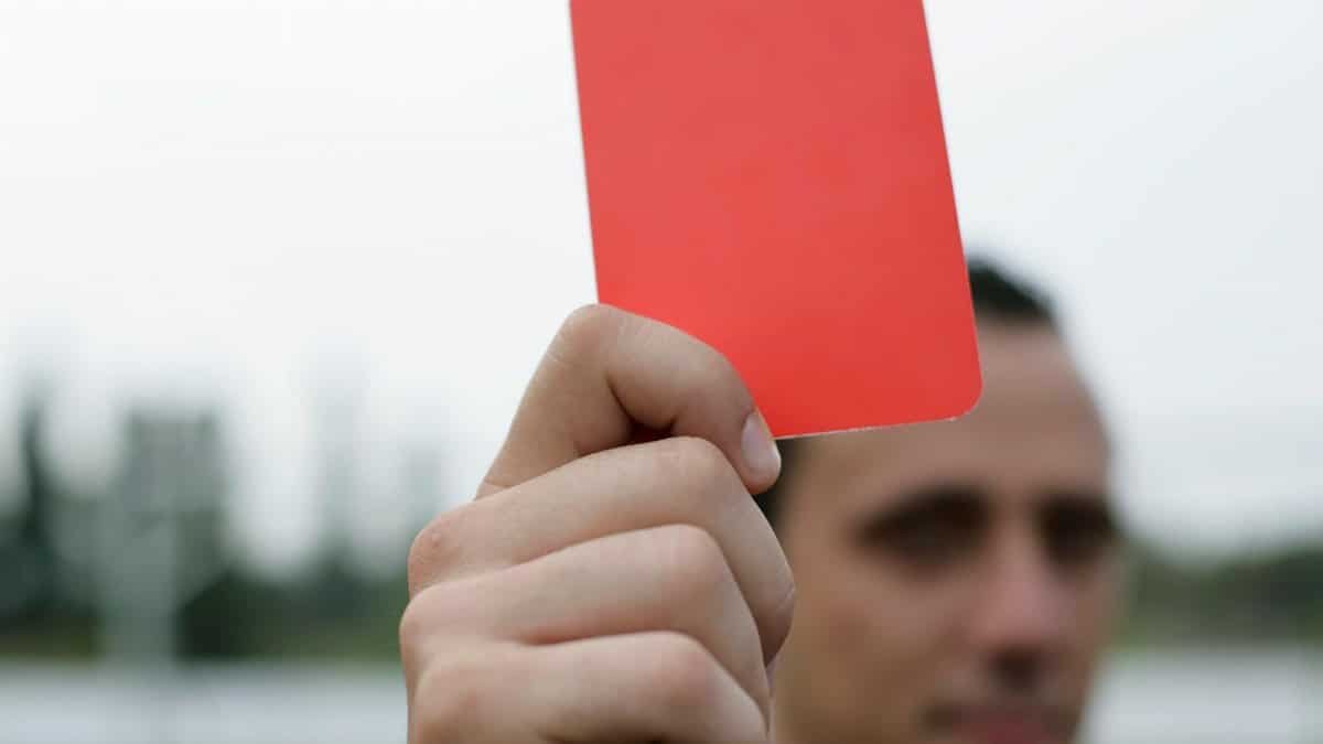 Close-up of a referee holding a red card, signaling a penalty in a soccer match.