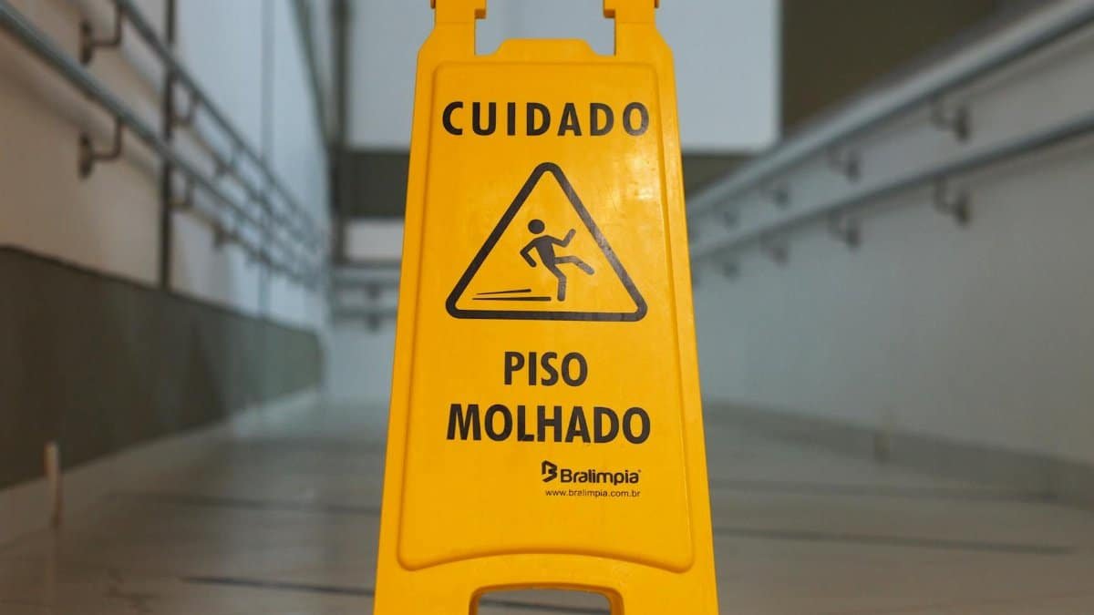 Bright yellow caution sign signals wet floor in a corridor with tiled flooring.