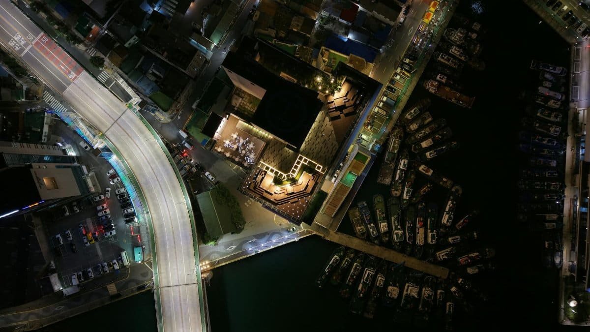 A captivating aerial image of Busan's cityscape at night, featuring illuminated roads and docked boats.