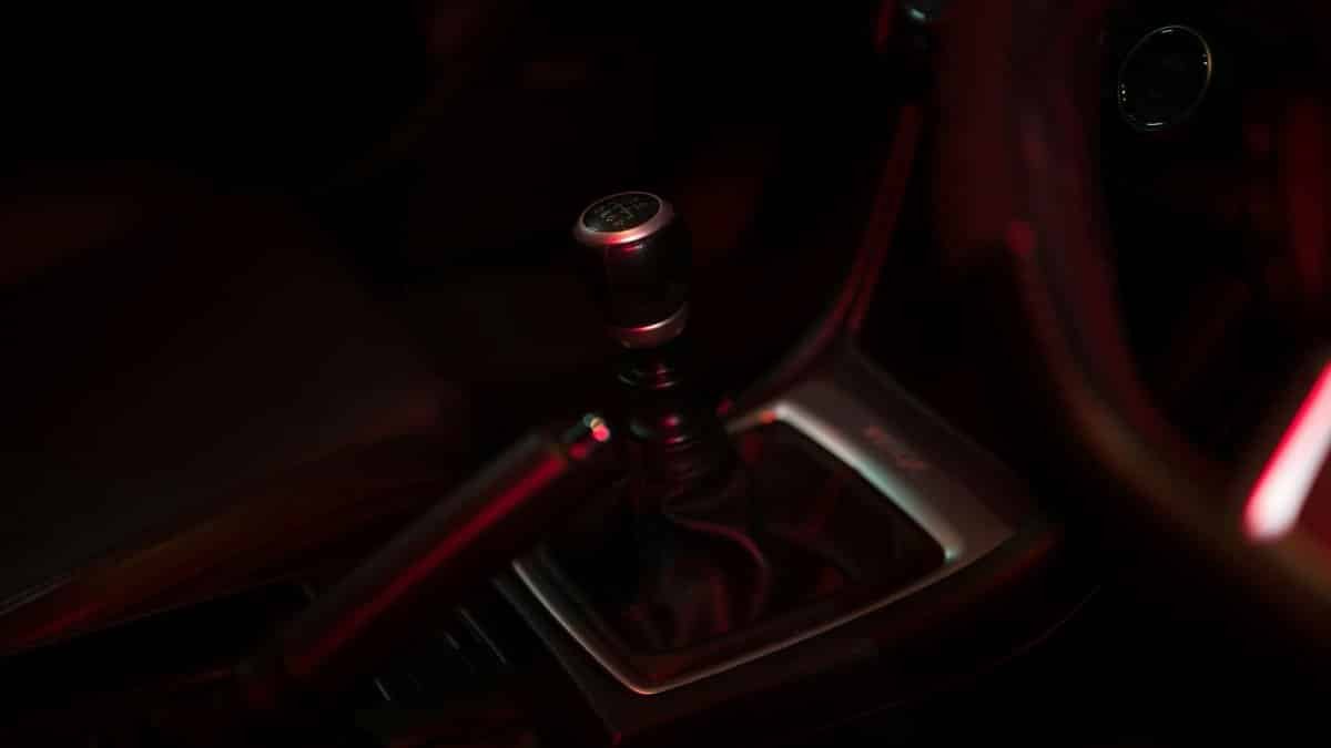 Detailed view of a manual gear shift in a dimly lit car interior, showcasing sleek design.
