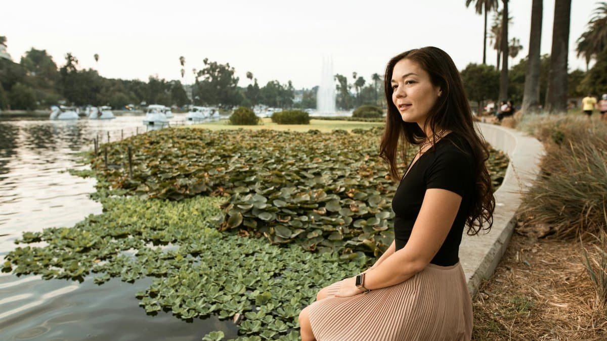 A woman sits by a serene lake filled with waterlilies, embodying tranquility.