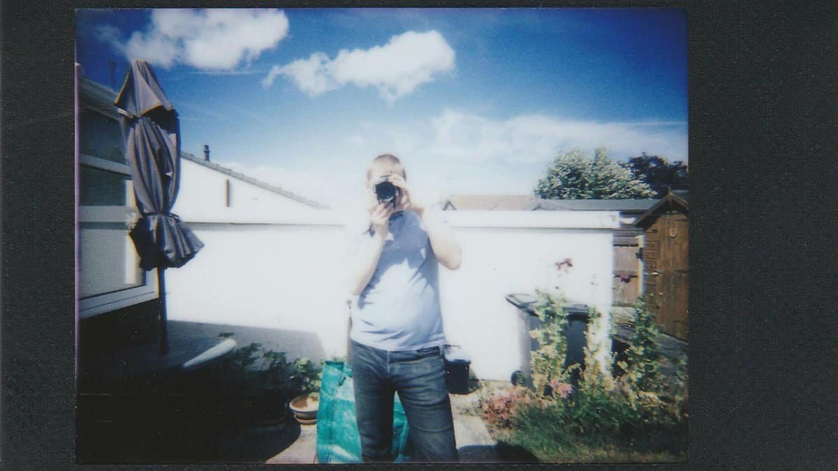 A man captures a photograph in a sunny backyard setting using instant film.