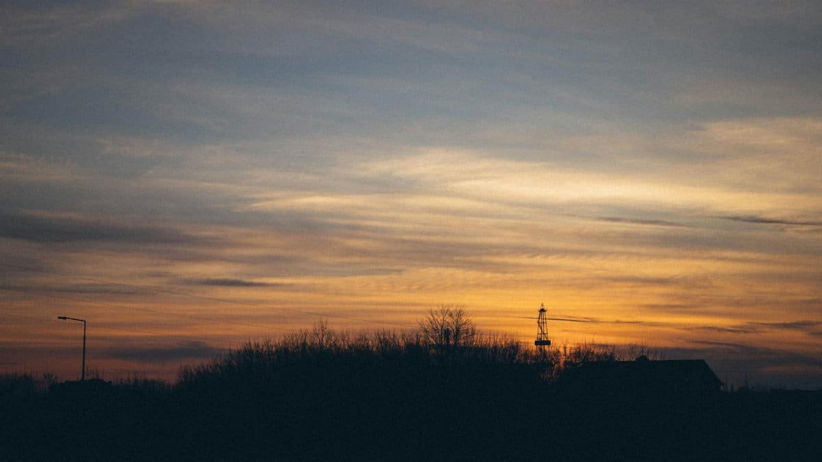 A calm sunset scene with silhouettes of houses and trees against a colorful sky.