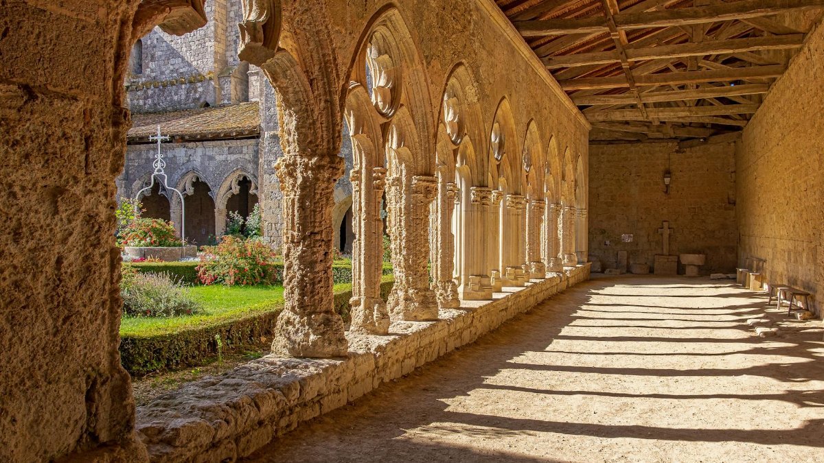 Experience the serene beauty of a historic cloister in La Romieu, bathed in sunlight and shadows.