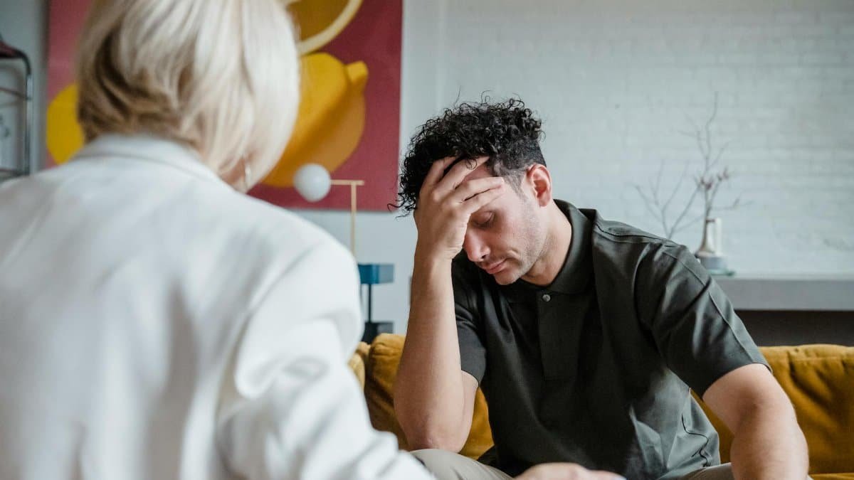 A young man in a therapy session, expressing emotions with hand on forehead.