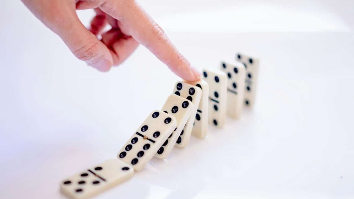 A close-up shot of a hand pushing dominoes, illustrating cause and effect.