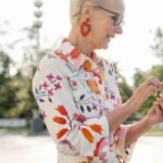 Smiling senior woman in floral dress using smartphone outdoors on sunny day.