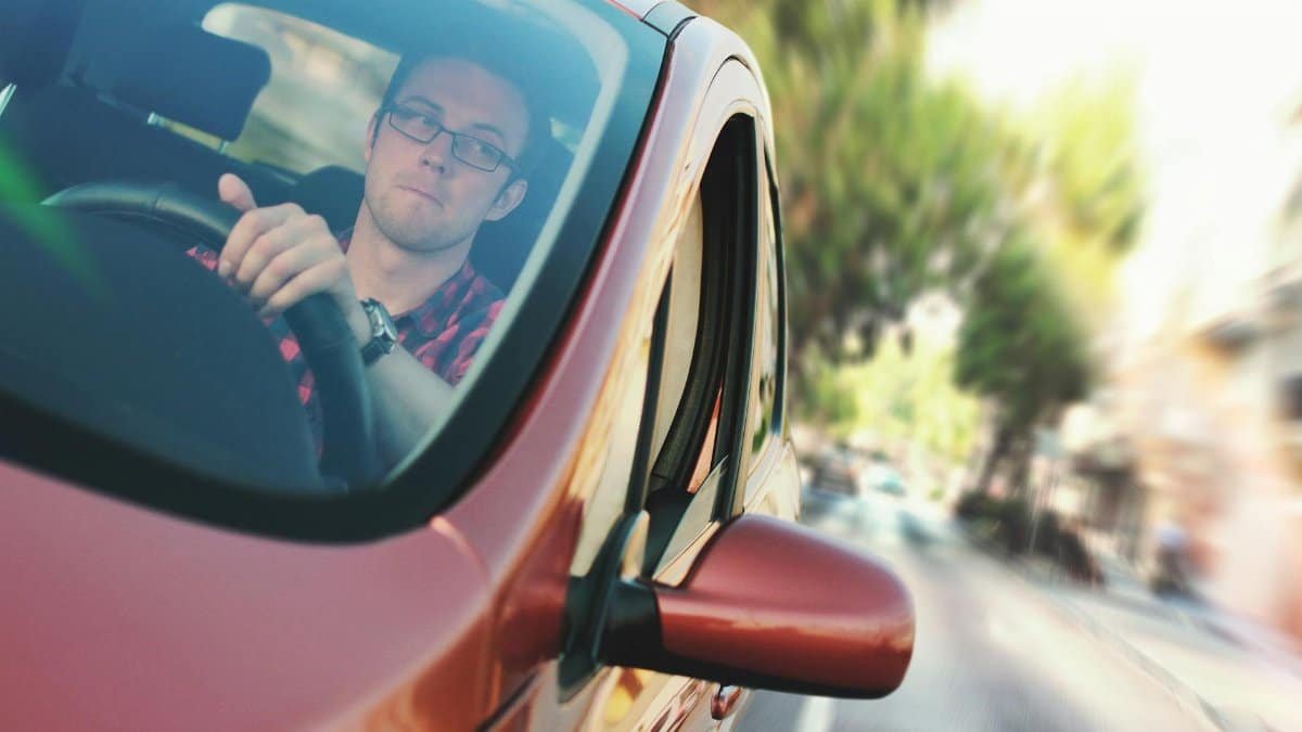 A man driving fast through a city street in a red car, showcasing motion and focus.