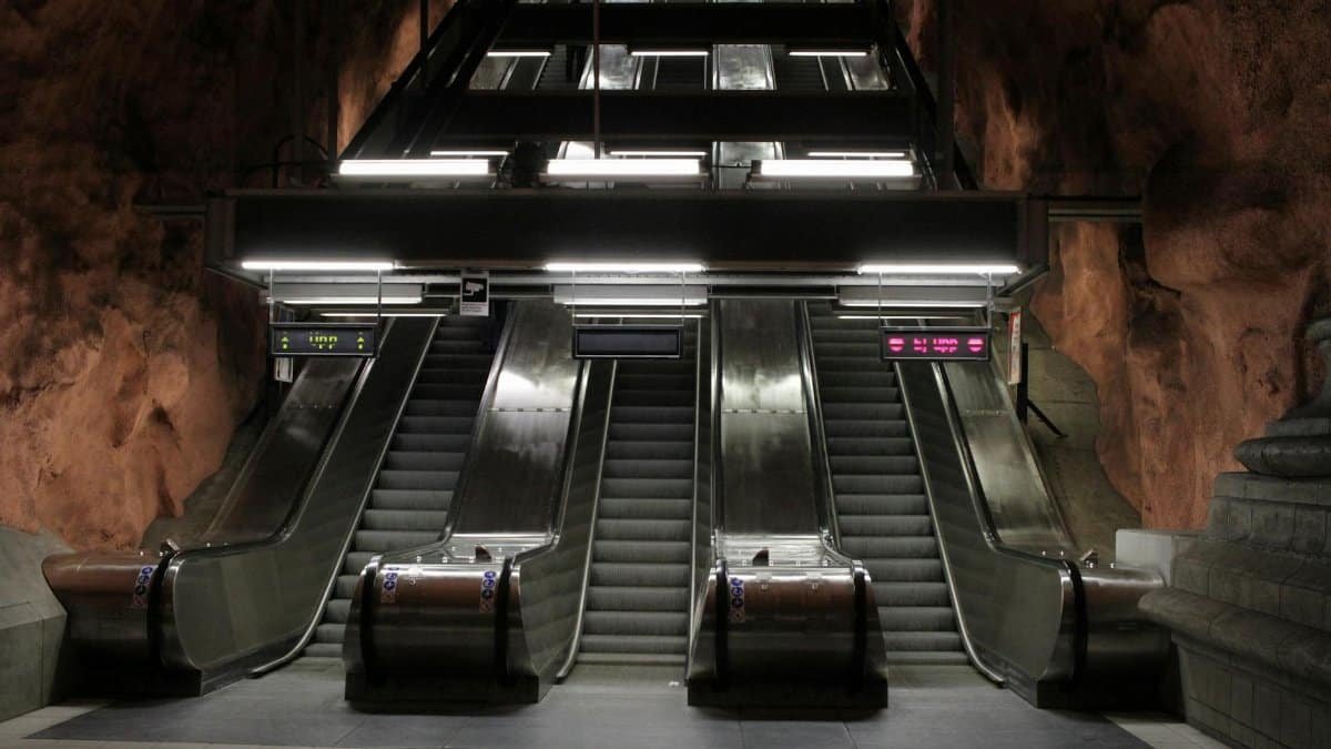 A modern escalator system inside a Stockholm subway station with rock walls.