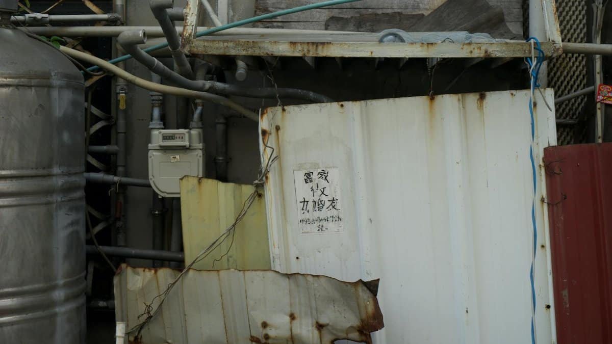 Close-up of rusty metal panels and exposed industrial pipes in an urban area.