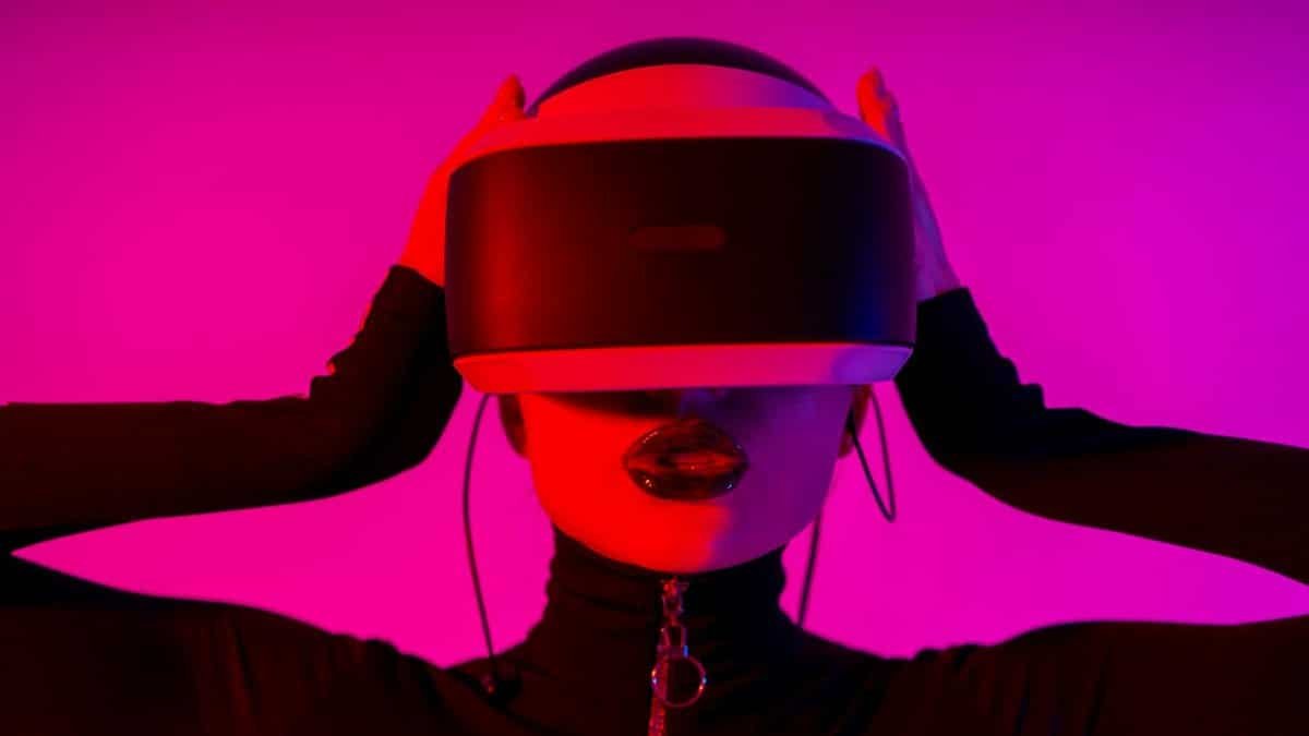 Astonished young female using virtual reality goggles while experiencing invisible reality on pink background