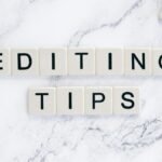 Scrabble tiles spell out 'Editing Tips' on a marble background, perfect for editorial guides.