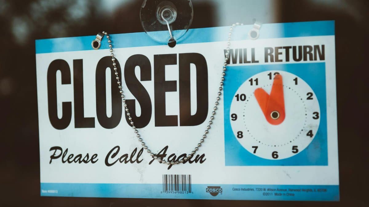 A close-up view of a 'Closed' sign on a door, displaying a return time.