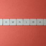 Minimalist photo of keyboard tiles spelling 'DOWNLOAD' on a red background.