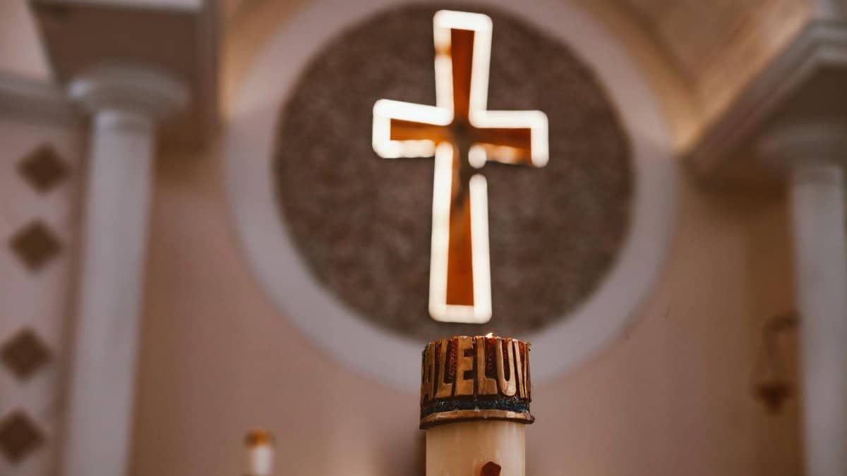 A glowing cross above an 'Alleluia' candle in a church, symbolizing faith and worship.