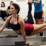 A young woman exercising in a São Paulo gym, performing Pilates moves on a reformer.