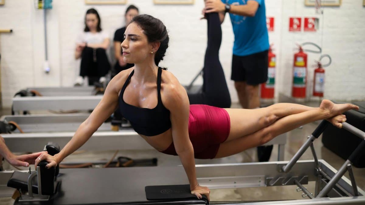 A young woman exercising in a São Paulo gym, performing Pilates moves on a reformer.