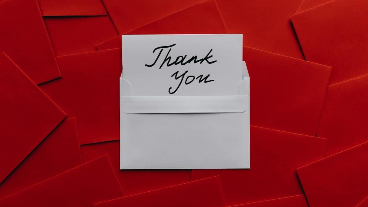 Elegant thank you card in white envelope on vibrant red envelopes flatlay. Perfect for gratitude themes.