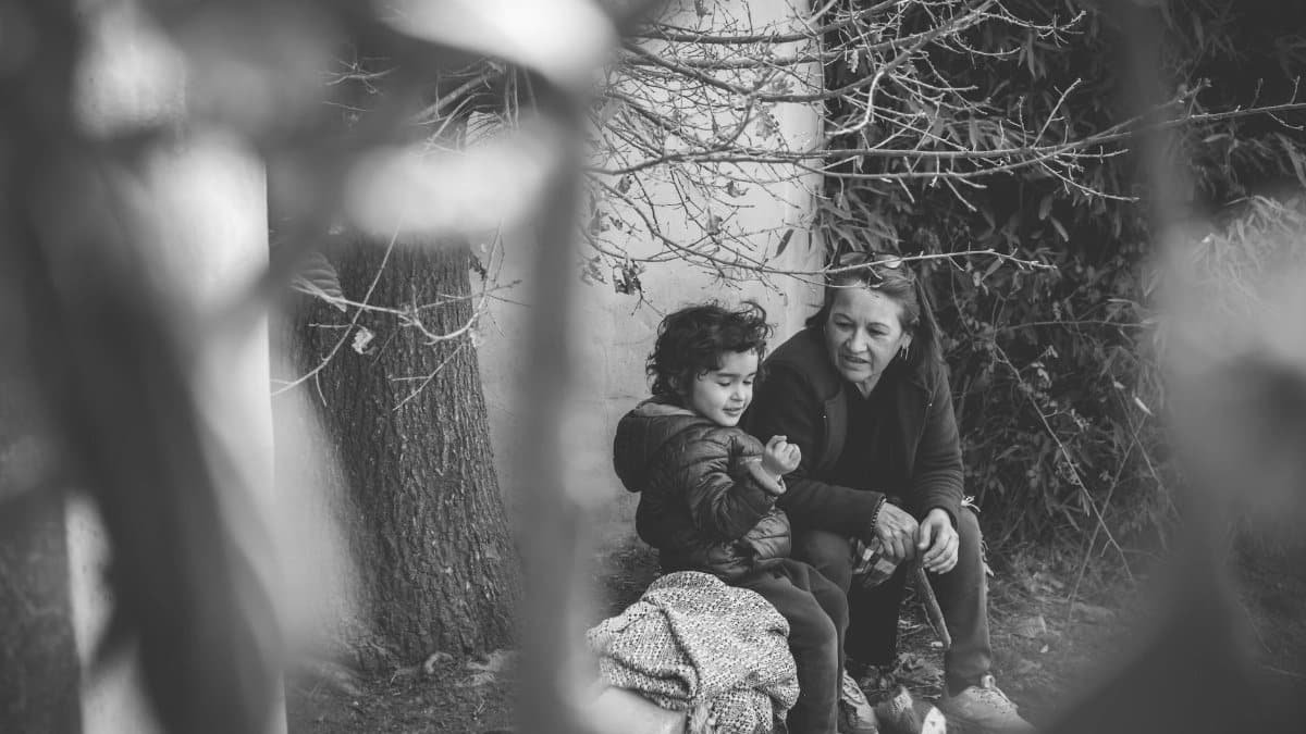A black and white photo capturing a tender moment between a child and an adult seated outdoors.