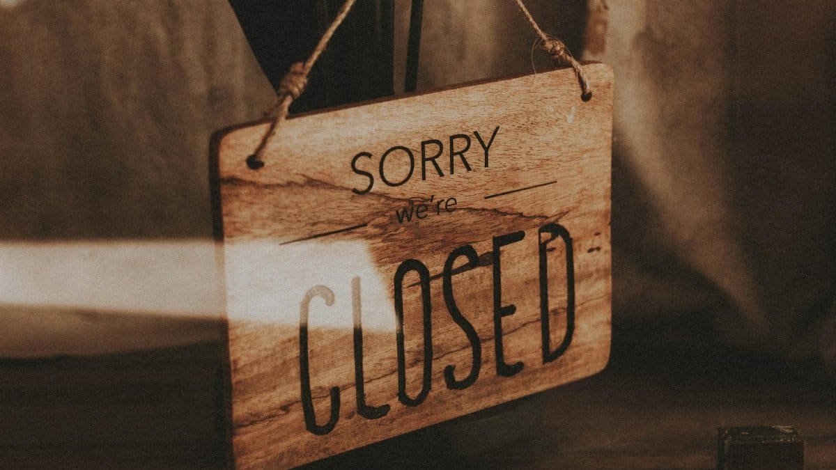 Through glass of wooden signboard with inscription Sorry We Are Closed hanging on doors of shop