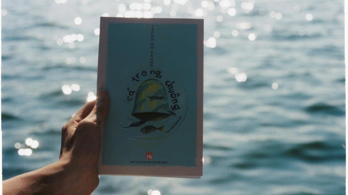 A hand holds a book against a backdrop of sparkling water, creating a calming scene.