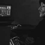 Monochrome image of a hacker in a Guy Fawkes mask working on a computer in a dimly lit room.