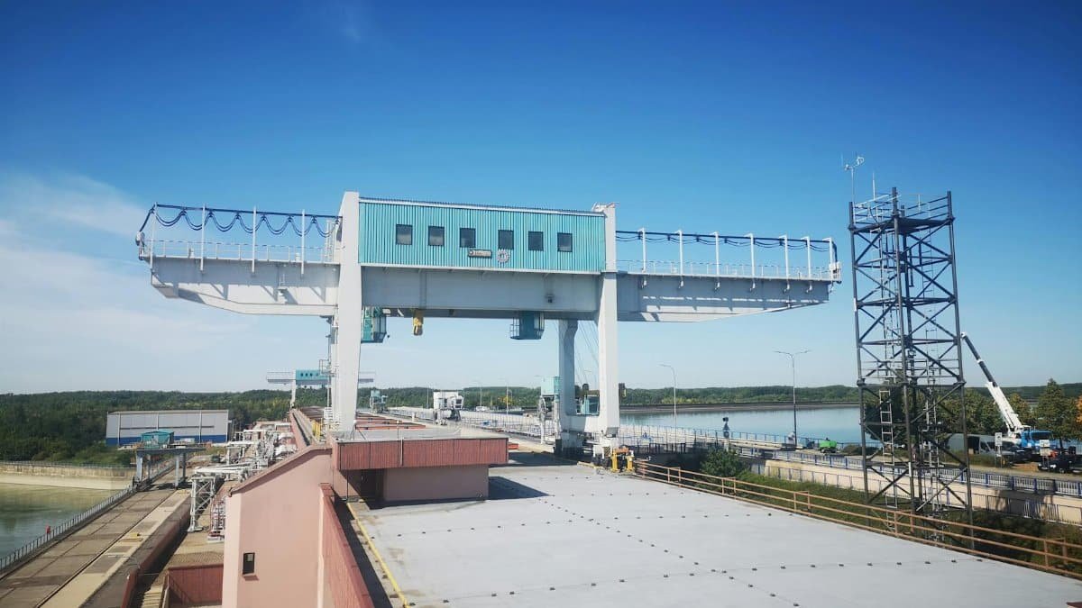 Blue skies over an industrial crane and structure near a river, showcasing modern engineering.