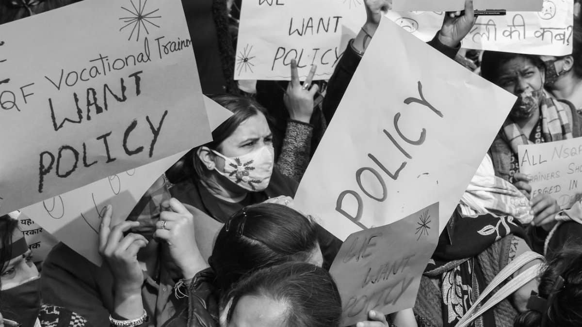 Black and white image of a protest with signs demanding policy changes for vocational trainers.