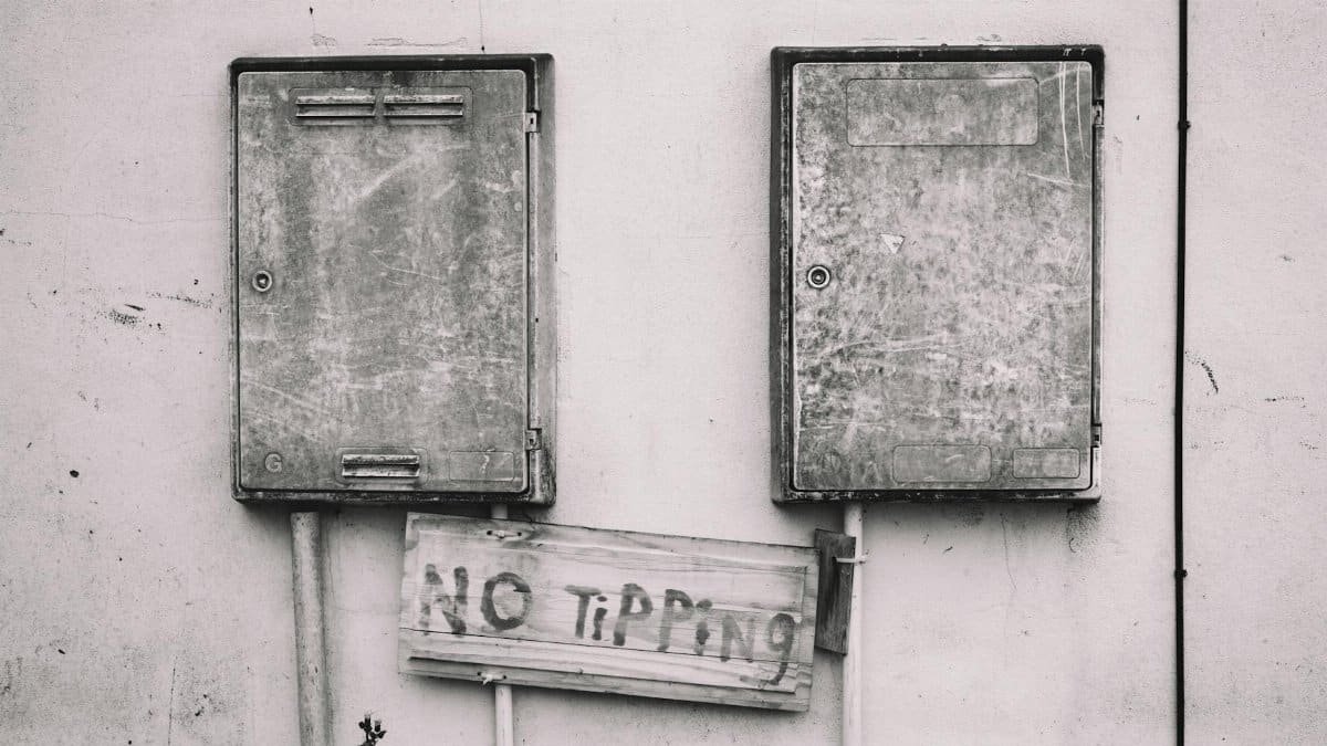 Black and white image of rusty electrical boxes with 'No Tipping' sign adds urban decay aesthetic.