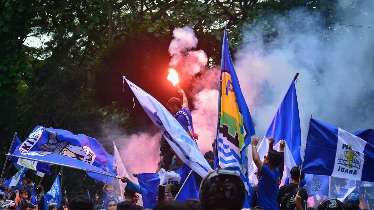 Excited football fans wave flags and light flares in a lively celebration in Bandung, Indonesia.