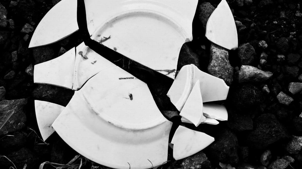 A shattered white ceramic plate lying on dark, textured rocks.